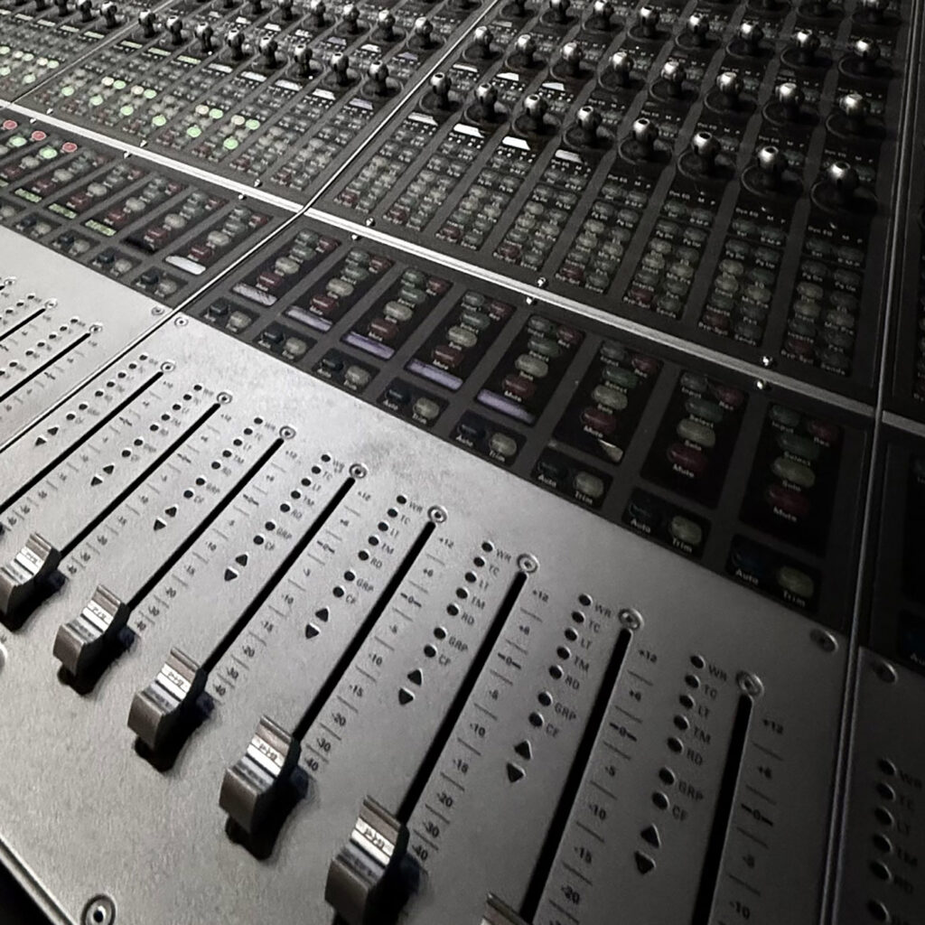 Close-up of a professional audio mixing console with numerous switches and sliders. The sleek, metallic surface conveys a sense of precision and technology.
